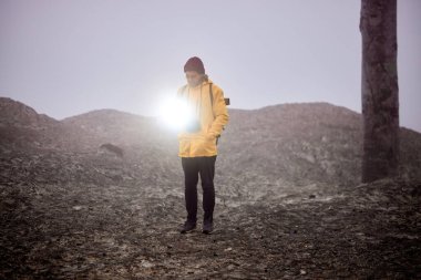 İnsan siste kayanın üzerinde durur ve karanlığa doğru keskin ışık sinyalleri gönderir.