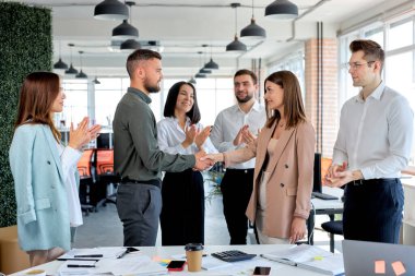 İki genç iş adamı modern ofiste meslektaşlarıyla el sıkışıyor.