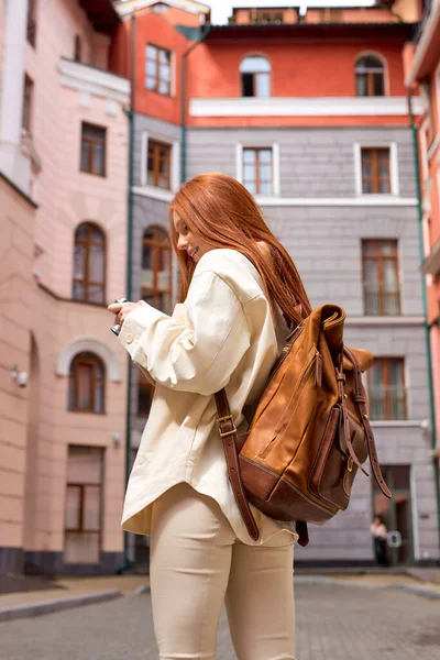 Bakifrån ung rödhårig resenär kvinna med kamera stående i en urban gata — Stockfoto