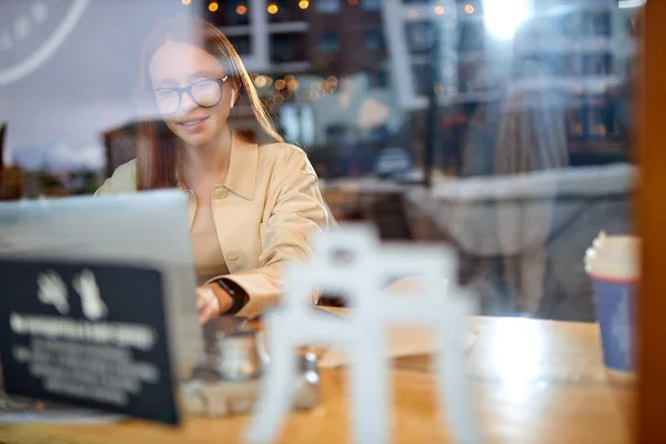 Vista attraverso finestra su femmina rossa in occhiali che lavorano in caffè su collaboratore esterno — Foto Stock