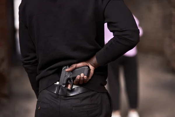 Вид ззаду на обрізаного злочинця в чорному светрі тримає пістолет, що стоїть за жінкою — стокове фото