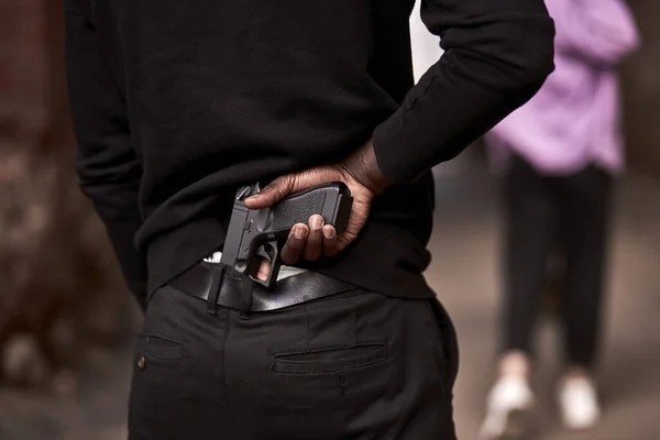 Ληστής ή εγκληματίας με μαύρη κουκούλα κρατάει όπλο πίσω από τη γυναίκα. — Φωτογραφία Αρχείου