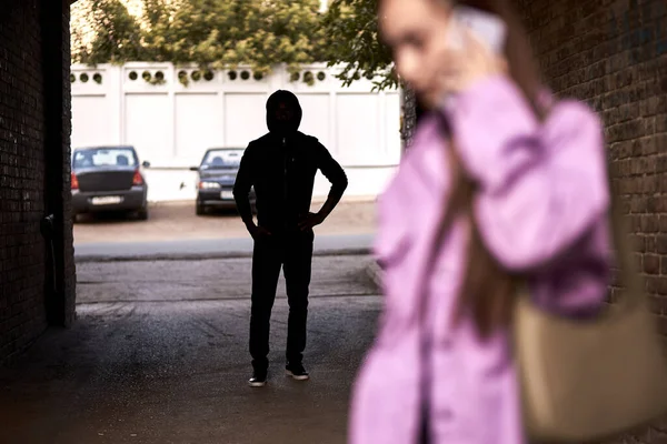 Злочинець переслідує жінку в темній вуличній алеї. Жінка розмовляє по телефону — стокове фото
