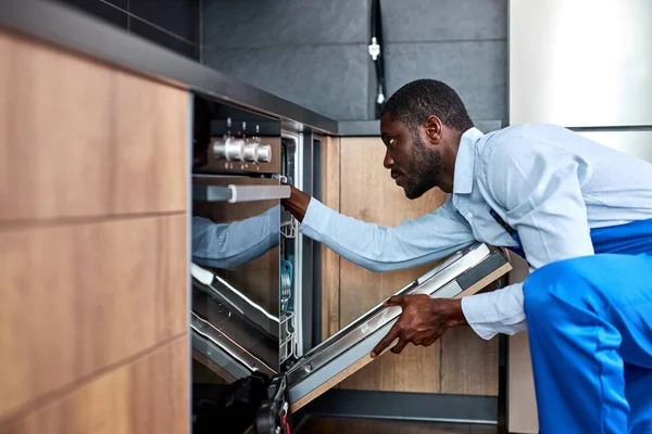 Vertrouwen s geschoolde Afrikaanse contractant in blauwe overall uniform gaat om Vaatwasser te repareren — Stockfoto