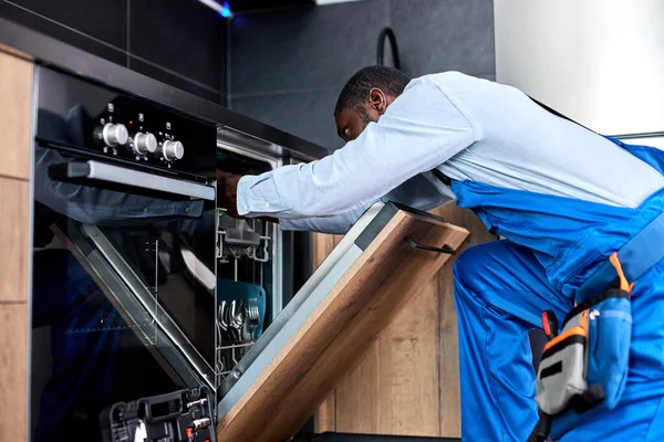 Профессиональный человек или обслуживающий персонал в специальной одежде устанавливает, разбирает посудомоечную машину — стоковое фото