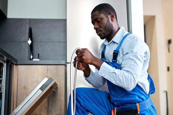 Serieuze Zwarte Handyman Repareren Vaatwasser, Noodzaak om oude vaatwasmachine slang te vervangen — Stockfoto