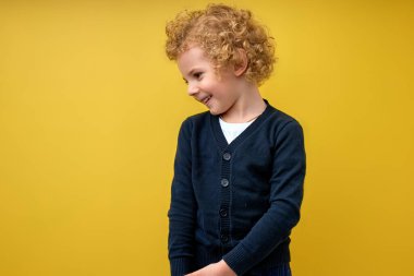 Sarı stüdyo arka planında yalnız poz veren iyi bir anaokulu çocuğu. Kıvırcık çocuk