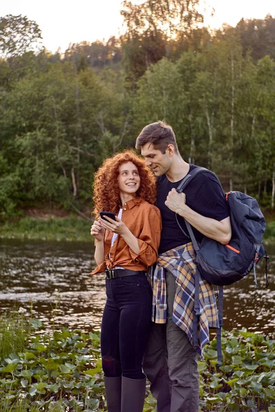 Lovely couple travelers standing by river using smartphone, olhando para o mapa online — Fotografia de Stock