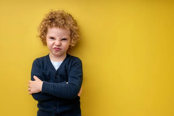 Niño dolorido con los brazos cruzados posando en la cámara, aislado en amarillo en el estudio — Foto de Stock