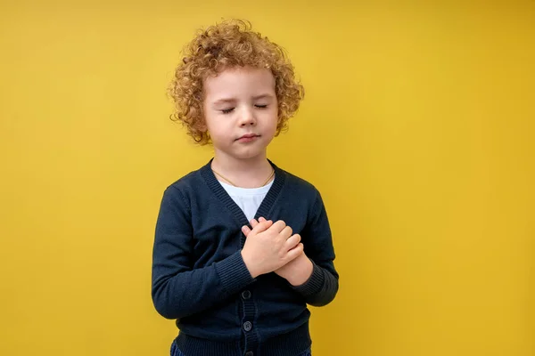 Lugn pojke hålla händer på bröstet med slutna ögon och tacksam gest i ansiktet — Stockfoto