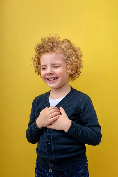 Niño alegre sosteniendo las manos en el pecho con los ojos cerrados y gesto agradecido en la cara — Foto de Stock