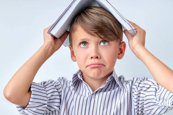 Школьник положил книгу себе на голову, глядя вверх, удивляясь. малыш веселится с домашним заданием — стоковое фото