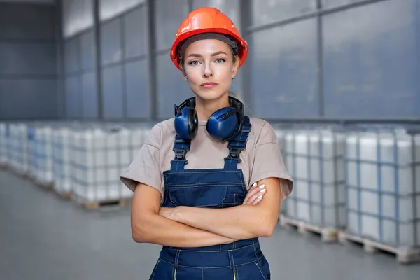 Serious industrial woman engineer in hardhat standing in factory with arms folded — Stock Photo, Image