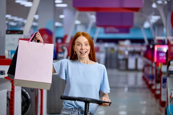Mulher dirigir scooter pontapé elétrico, feliz depois de fazer compras, desfrutar de andar em lojas na sexta-feira preta — Fotografia de Stock