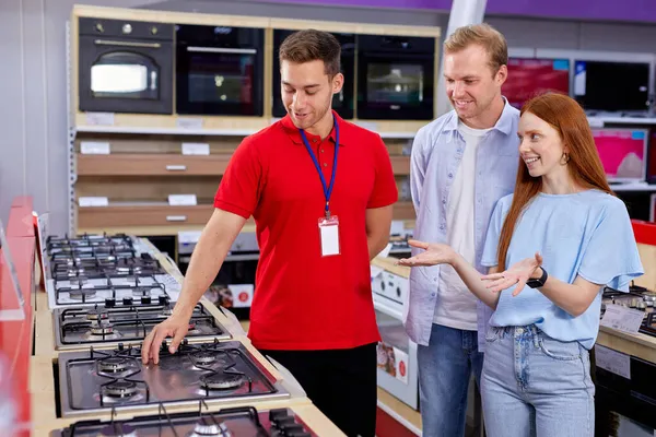 Мужчина и женщина выбирают плиту в магазине бытовой техники, разговаривают с консультантом — стоковое фото