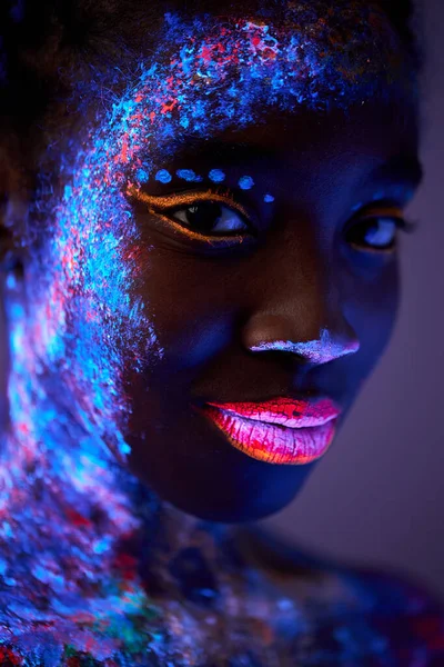 Negro señora con neón maquillaje cuerpo arte posando mirando cámara, aislado en púrpura —  Fotos de Stock