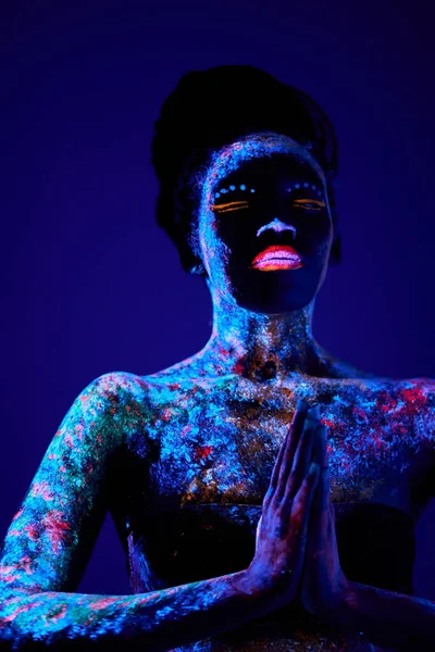 Mulher modelo preto em luz de néon, modelo com maquiagem fluorescente na posição de oração — Fotografia de Stock