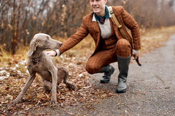 Jägarman med grå jakthund i skogen. man sitter och smeker hund på jakt utomhus — Stockfoto