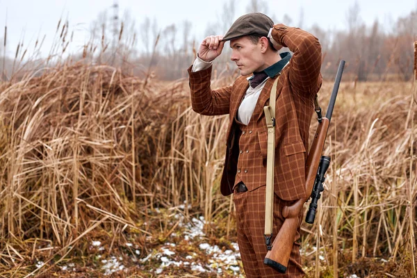 Hunter macho ajustar el sombrero, en traje. Cazador con arma de caza en la naturaleza, mira a un lado. —  Fotos de Stock