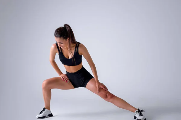 Jovem caucasiano mulher treinador em sporty preto short top e shorts de ginástica faz lunges — Fotografia de Stock