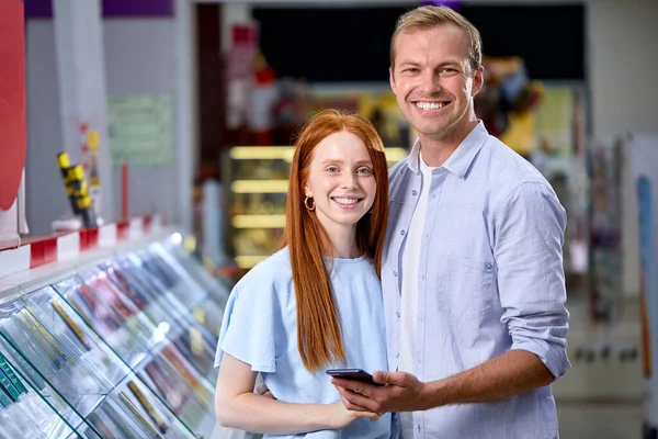 Jovem alegre e mulher verificando telefone celular na loja de tecnologia. — Fotografia de Stock