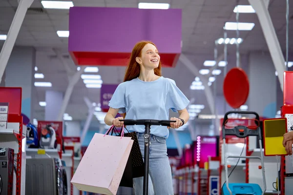Lady drive scooter elétrico pontapé, feliz depois de fazer compras, desfrutar de andar em lojas na sexta-feira preta — Fotografia de Stock