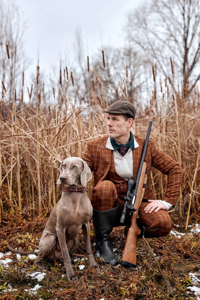 Confident american hunter man with dog holding shotgun rifle walking in countryside