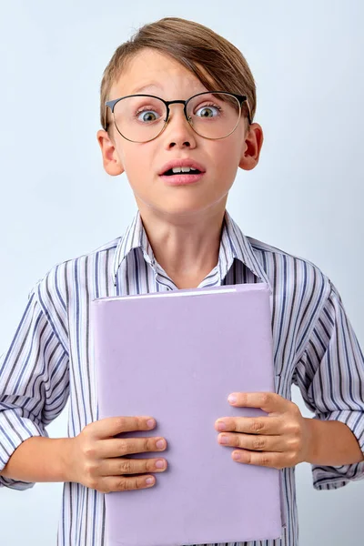 Емоційний хлопчик в окулярах тримає книгу, шокований і боїться помилки. здивований вираз — стокове фото