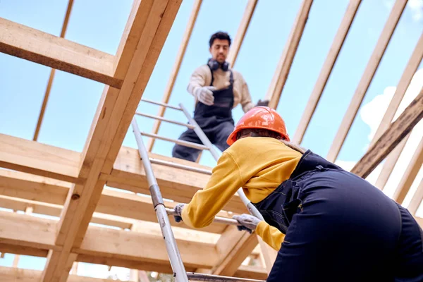 Zwei Bauunternehmer klettern auf Leiter auf Dach von Holzhaus — Stockfoto