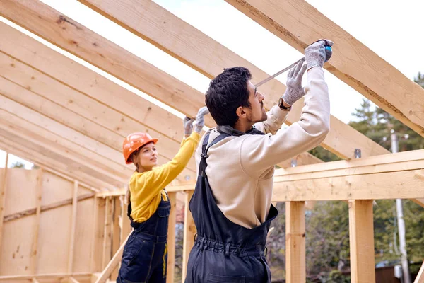 Réparation de toit en bois à l'extérieur. Deux constructeurs en vêtements spéciaux travaillent dans une maison neuve. — Photo