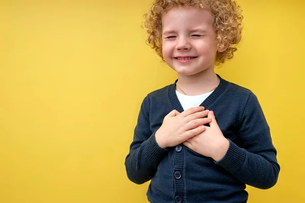 Vreugdevolle jongen houdt handen op de borst met gesloten ogen en dankbaar gebaar op gezicht — Stockfoto