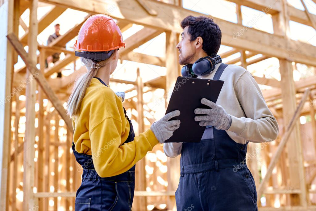 skilled man and woman in uniform and helmet explore construction documentation