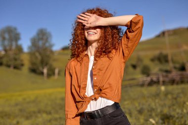 Güzel kızıl saçlı kadın yüzünü güneşten gizler. Akşam vakti doğada, ormanda arka planda.