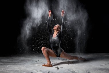 Zarif balerin kadın dans ediyor ve siyah arka planda un serpiyor.