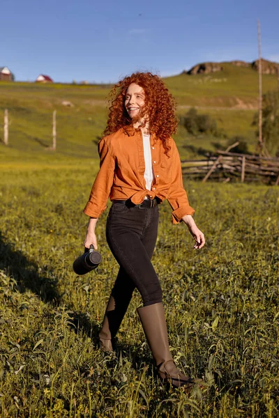 Reiseleiterin. schöne junge kaukasische Frau zu Fuß auf dem Feld mit Thermoskanne — Stockfoto