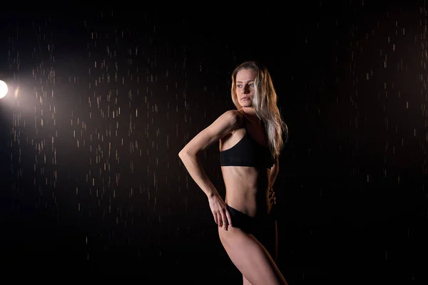 Blonde young lady posing under drops of water, isolated on black background — Stock Photo, Image