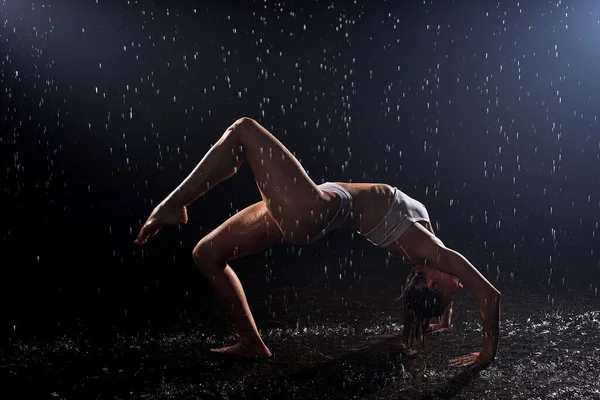Silhouette de jeune femme humide sexy en maillot de bain dansant sur le sol sous la pluie et les éclaboussures — Photo