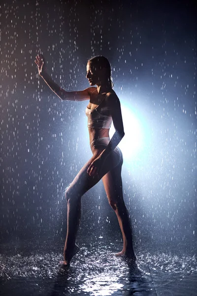 Slim female dancer is standing under rain as statue, posing in darkness, wet sexy body — Stock Photo, Image