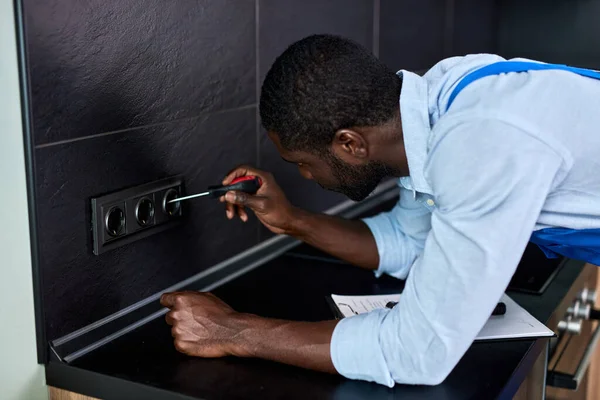 Zwarte afro Elektricien reparatie van stopcontacten van residentieel elektrisch systeem, met behulp van schroevendraaier — Stockfoto