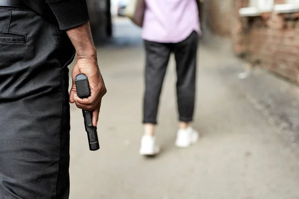 Vista trasera en el hombre recortado llevando pistola y siguiendo a la joven mujer caminando en la calle —  Fotos de Stock