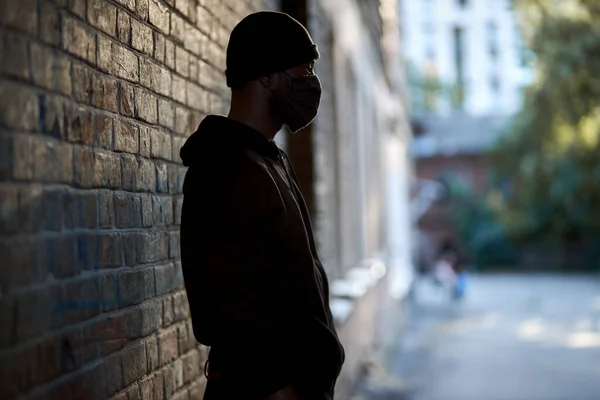 Joven negro enmascarado de pie en la calle esperando a la víctima, mirando al lado — Foto de Stock