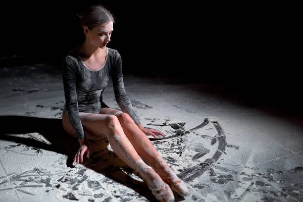 Vue latérale de la jeune danseuse de ballet épuisée en body assise sur le sol — Photo