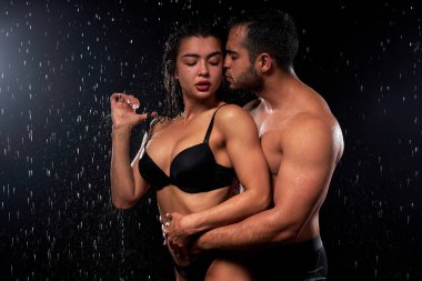 Zinde ve tutkulu romantik çift siyah arka planda su damlalarında sarılıyorlar.