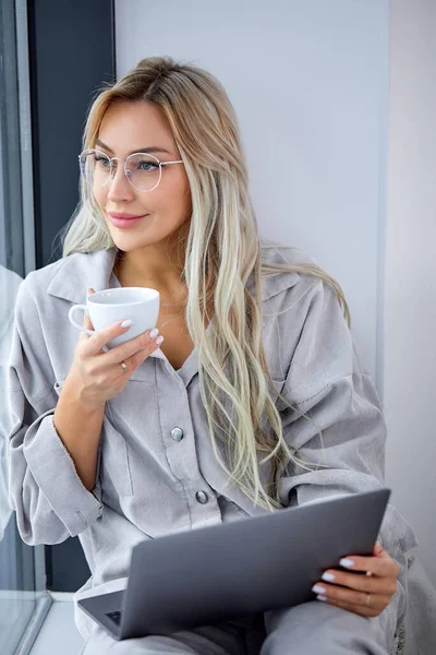 Очаровательная женщина в повседневной одежде с помощью компьютера ноутбука и сидя на подоконнике — стоковое фото