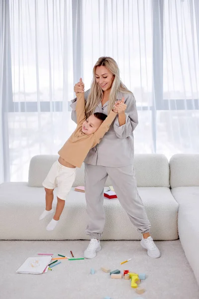 Cheerful young playful mother raising child up, imitate fly with small son. — Stock Photo, Image