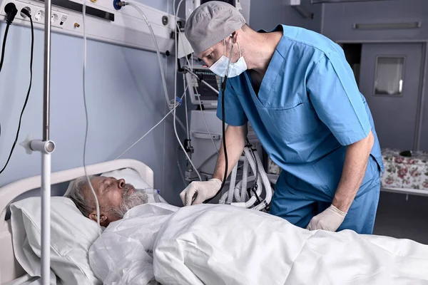 Säker manlig sjuksköterska sätta stetoskop till senior patient, kontrollera hjärtslag. — Stockfoto