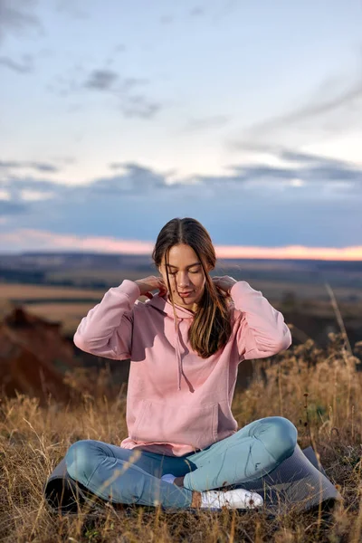 Mujer joven se dedica al yoga, sentado en la colchoneta de fitness al aire libre. concepto de bienestar — Foto de Stock