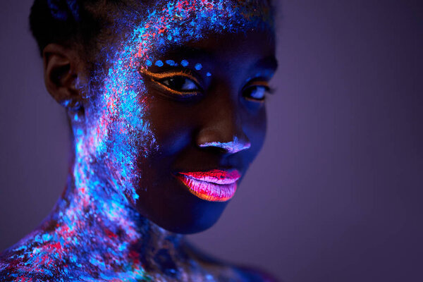 black female with body art in ultraviolet light. woman painted in fluorescent powder