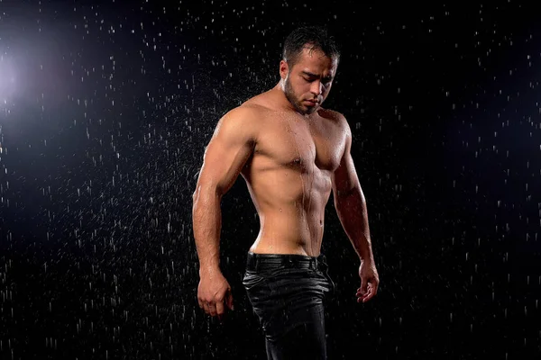 Vista lateral del culturista hombre en forma posando en la cámara, de pie bajo la lluvia. Deportivo muscular chico —  Fotos de Stock