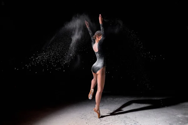Bailarina de ballet flexible mujer bailando y espolvorear harina sobre fondo negro — Foto de Stock